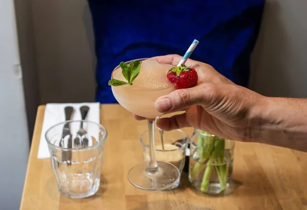 Mano maschile in possesso di un cocktail con fragola e foglia di menta con uno sfondo sfocato — Foto Stock