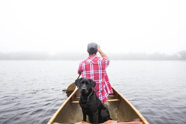 Siyah bir köpek ve su gövdesi üzerinde küçük bir tekne üzerinde yelken bir erkek güzel atış — Stok fotoğraf