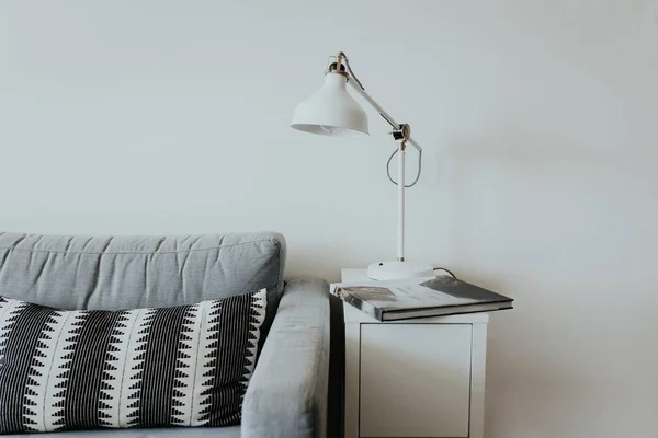 Wygodna kanapa w nowoczesnym domu z lampką na małej białej półce i książkę z wodospadem — Zdjęcie stockowe