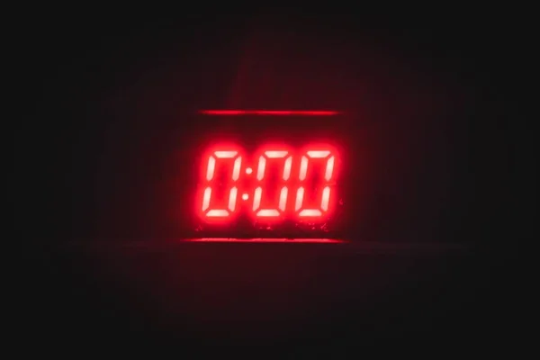 Gece yarısını gösteren koyu bir arka plan üzerinde kırmızı neon numaraları "0:00" ile dijital saat — Stok fotoğraf