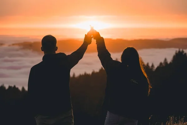 A silhouette of a couple holding hands and standing on top the mountain Tam near a sea at sunset in San Francisco, CA.
