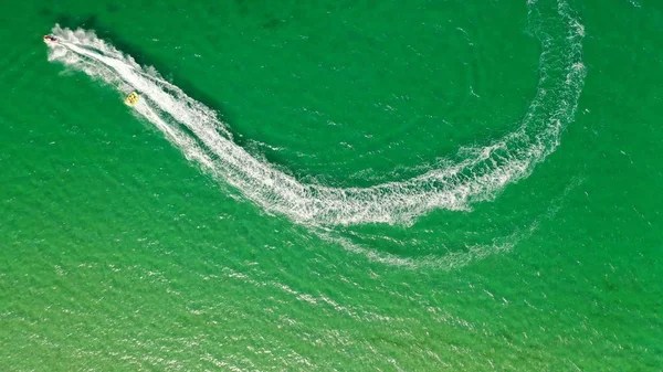 An aerial overhead shot of a boat with a person surfing on a rope attached to it