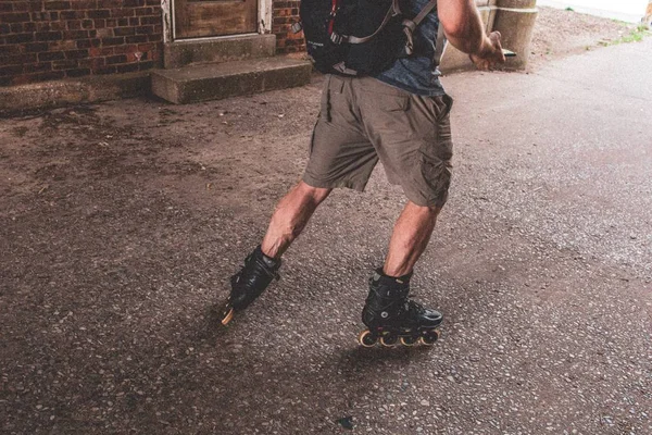 Slightly closeup shot of a male skating wearing black roller skates, shorts and  backpack — Stock Photo, Image