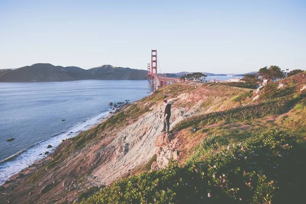 Uçurumun kenarında duran erkek denize ve Golden Gate köprüsüne bakıyor. — Stok fotoğraf