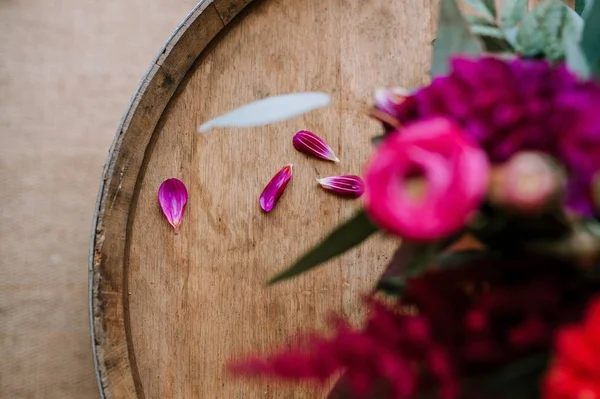 Wooden barrel with flower petals on it and a bouquet in a blur in the foreground
