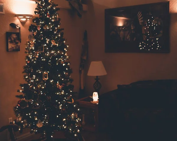 Hermosa foto de un árbol de Navidad con adornos y luces cerca de imágenes y marcos en una pared —  Fotos de Stock