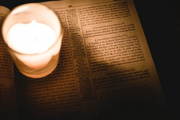 Verlichte kaars in een pot op een bijbelboek geschreven in het Spaans in een donkere kamer — Stockfoto