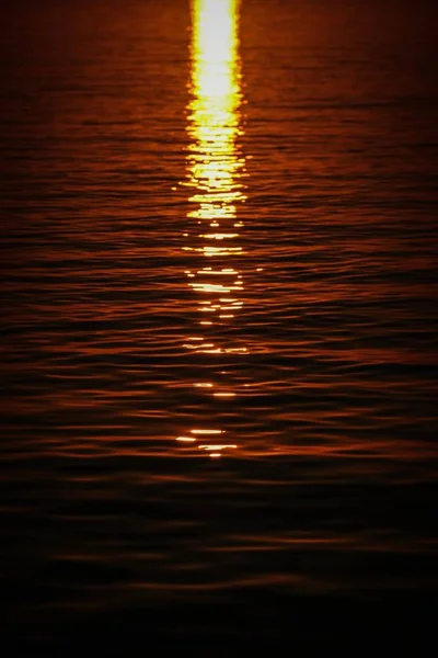 Tiro vertical das ondas do mar que refletem a luz solar ao pôr do sol — Fotografia de Stock