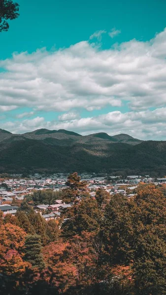 Una ciudad rodeada de árboles y montañas bajo un cielo azul claro con nubes blancas —  Fotos de Stock