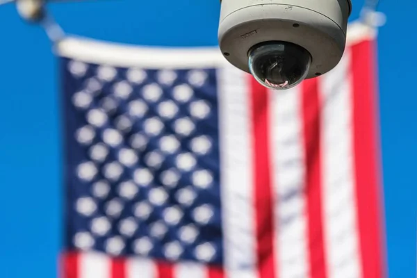 Выборочный фокусный снимок камеры безопасности с размытым американским флагом на заднем плане — стоковое фото