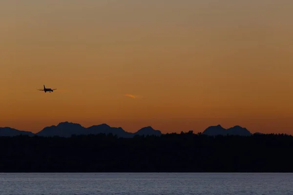 Vliegtuig dat bij zonsondergang over heuvels en zee vliegt — Stockfoto