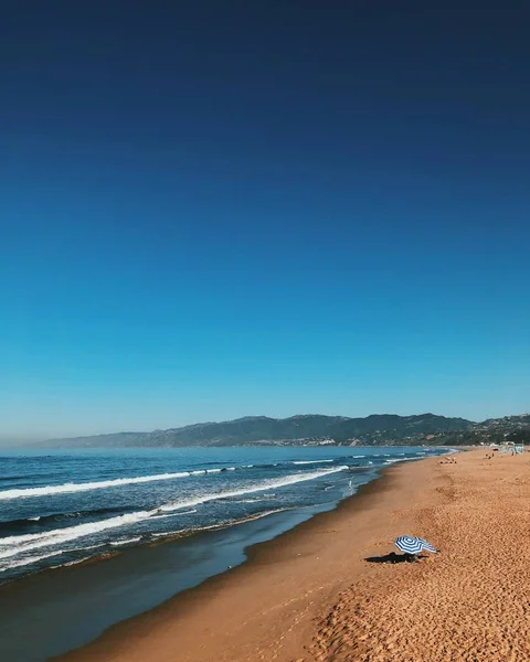 Bellissimo ampio scatto di una spiaggia sabbiosa con due ombrelloni e sorprendente cielo azzurro chiaro — Foto Stock