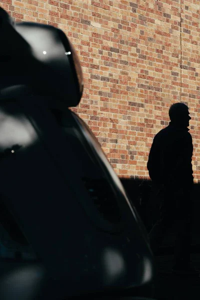 Silhueta de uma pessoa misteriosa em pé na frente de uma parede de tijolo em um estacionamento — Fotografia de Stock