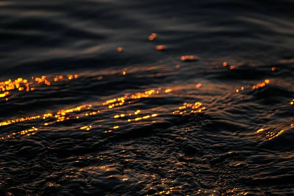Närbild av ett hav med vågor som reflekterar solen vid solnedgången — Stockfoto