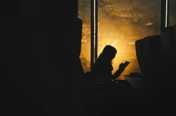 Silhouet van een vrouwtje dat iets leest op een stoel met een oranje, heldere achtergrond — Stockfoto