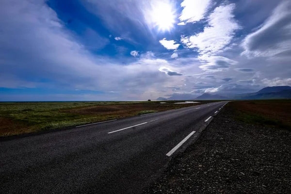 Bella ripresa di una strada in mezzo a un campo con montagne in lontananza sotto un cielo nuvoloso — Foto Stock