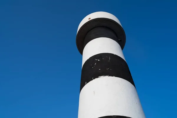 Low angle shot of a white and black striped lighthouse beacon tower with a sky blue background — Stock Photo, Image