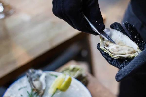 Closeup shot of a chef's hands opening an oyster with a blurred background — Stock Photo, Image