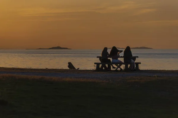 Gün batımında deniz kıyısında bir masanın etrafında oturan üç kadın güzel atış — Stok fotoğraf