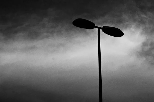 Baixo ângulo de tiro de uma lâmpada de poste em preto e branco com um fundo nublado — Fotografia de Stock