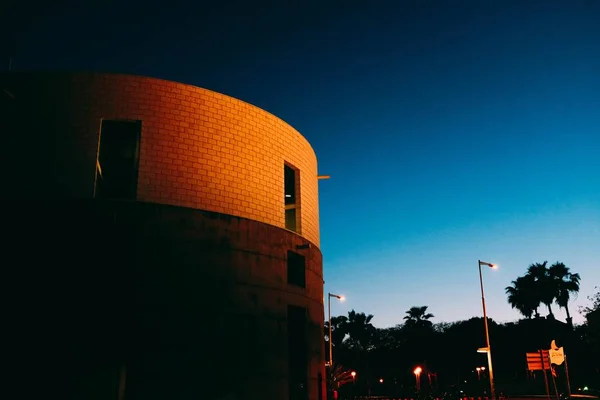 Низкий угол съемки круглого кирпичного современного здания с солнцем, сияющим на нем на рассвете — стоковое фото