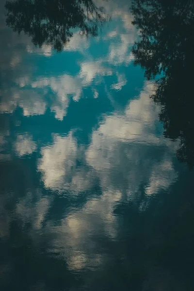 Vertikale Aufnahme von Wasser, das den blauen Himmel mit Wolken und Bäumen reflektiert — Stockfoto