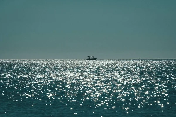 Vue à longue distance d'un bateau naviguant sur la mer reflétant le soleil avec un ciel bleu clair en arrière-plan — Photo