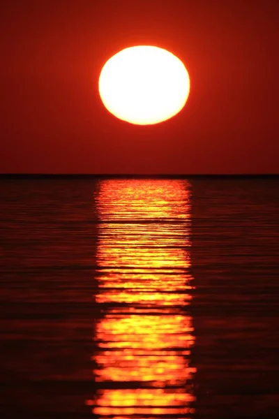 Vertikale Aufnahme des Meeres, das die Sonne mit dem roten Himmel bei Sonnenuntergang reflektiert — Stockfoto