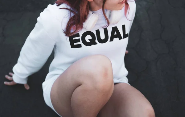 Junge attraktive Frau auf dem Boden sitzend mit einem Hemd, auf dem "EQUAL" steht — Stockfoto