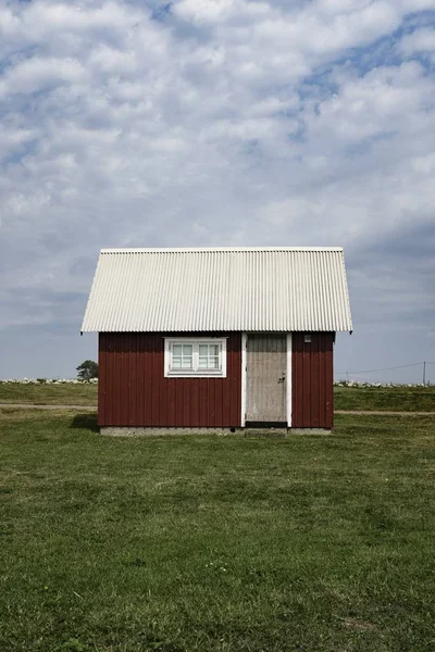 Houten rode schuur met een wit dak in een groot groen veld met bewolkte blauwe hemel — Stockfoto