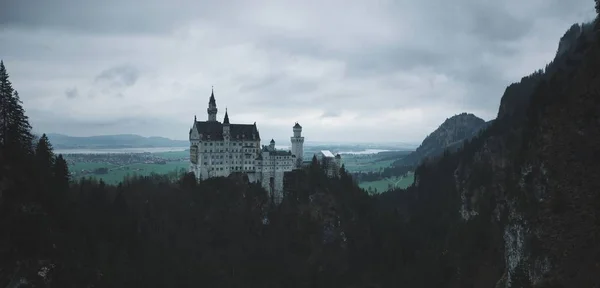 Panoramic shot of Neuschwanstein castle near mountains on a cloudy day — 스톡 사진