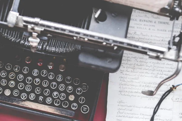 Closeup shot of an old vintage typewriter on a red desk with paper on the side — Stock Photo, Image