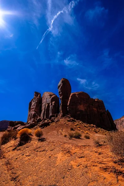 Tiro vertical de uma colina de deserto e grandes rochas na distância abaixo de um céu azul em um dia ensolarado — Fotografia de Stock