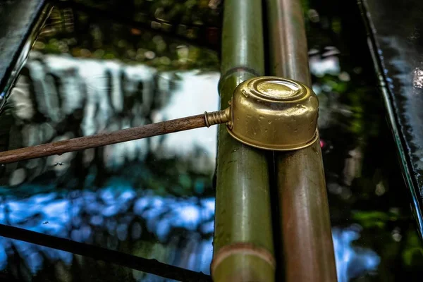 Close shot of a small pot with a long wooden handle leaned on bamboo over the water