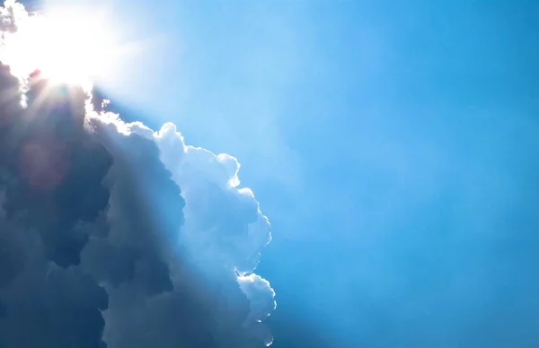Aufnahme der tief stehenden Sonne, die hinter den Wolken in einem hellblauen Himmel scheint — Stockfoto