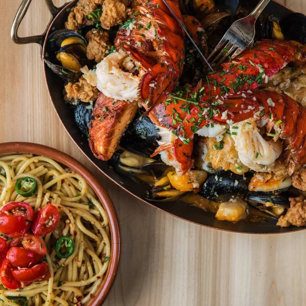 Overhead shot of pasta near a pan of fried lobster and meat with oysters on a wooden surface — Stock Photo, Image