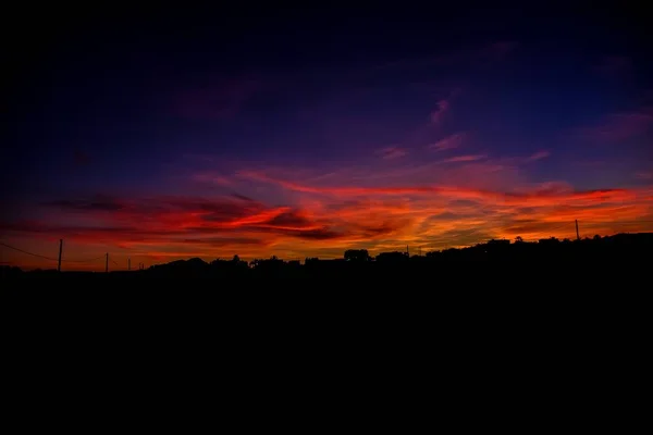 Silhouette di alberi ed edifici sotto un cielo viola e giallo un tramonto — Foto Stock