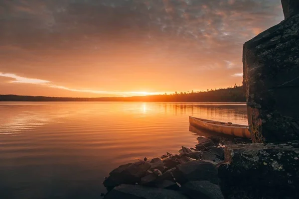Schöne Weitaufnahme eines Kanus auf einem See in der Nähe von Steinhügeln bei Sonnenuntergang — Stockfoto