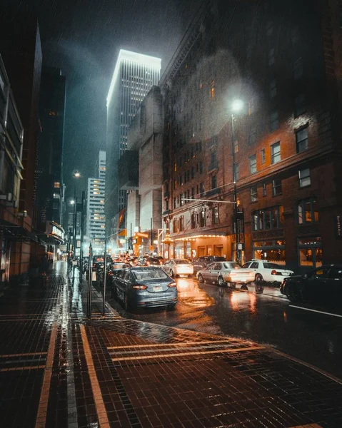 Vertical shot of buildings on a wet street with cars during nighttime — ストック写真