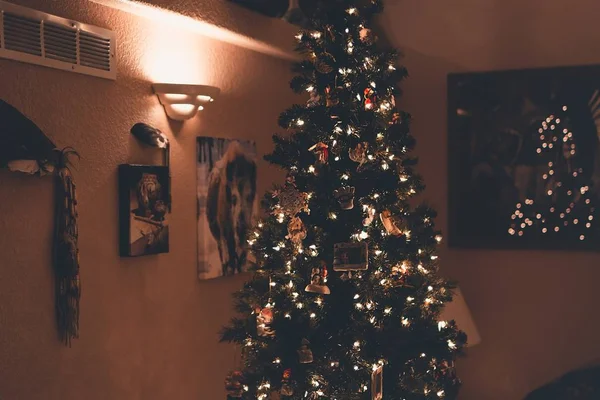 Hermosa foto de un árbol de Navidad con adornos y luces cerca de imágenes y marcos en una pared — Foto de Stock