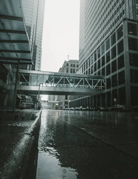 Vertical distant shot of a suspension bridge connecting two buildings in a wet highway — 스톡 사진