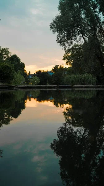 Colpo verticale di un lago circondato da alberi sotto un cielo durante il tramonto — Foto Stock