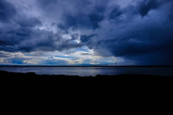 Silhouette eines grasbewachsenen Feldes am Meer unter wolkenverhangenem Himmel — Stockfoto