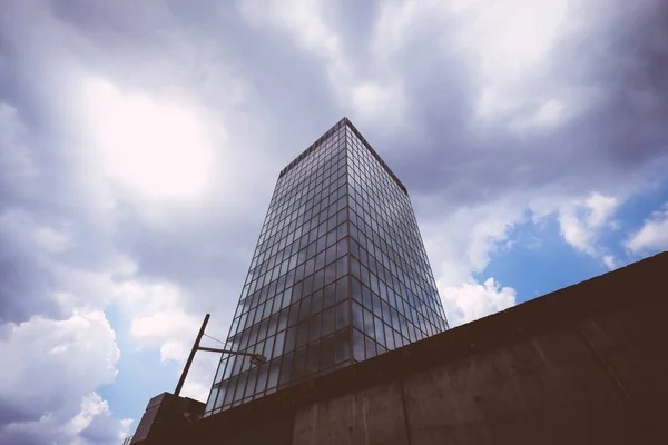 Colpo basso di un alto edificio di vetro con cielo nuvoloso sullo sfondo — Foto Stock