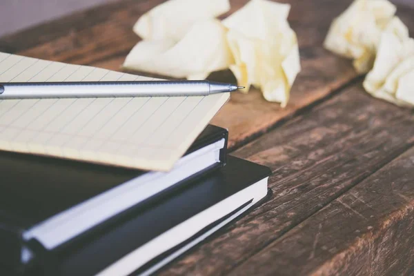 Primer plano de los libros de texto con una pluma gris y pedazos arrugados de papel alrededor de una superficie de madera — Foto de Stock