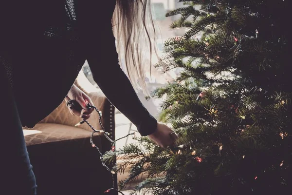 Interieur shot van een vrouwtje versierend de kerstboom tegen nieuwjaar avond — Stockfoto