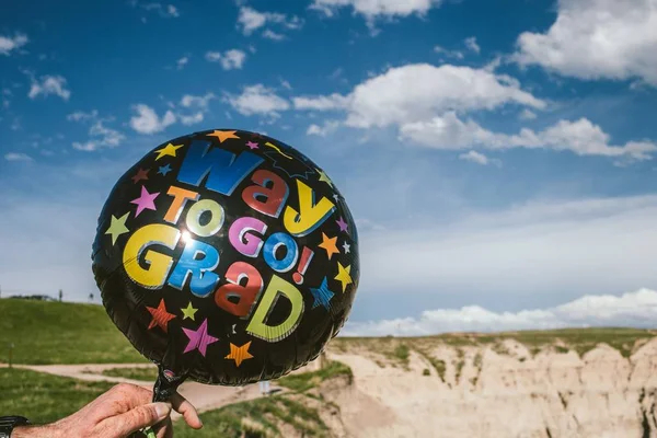 Крупный план черного воздушного шара с надписью "Way to go Grad", которую держит человек в пустыне — стоковое фото