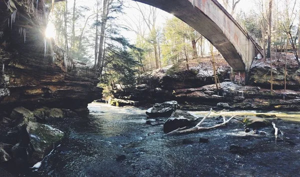 Breite Aufnahme von Wasser, das inmitten von Felsen und einer Brücke über den See an einem sonnigen Tag fließt — Stockfoto