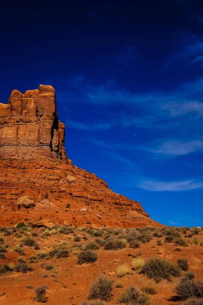 Colpo verticale di un deserto con cespugli secchi e una grande scogliera in lontananza sotto un cielo blu — Foto Stock