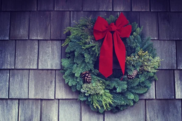 Closeup shot of a green Christmas wreath with a red ribbon on it on a wooden background
